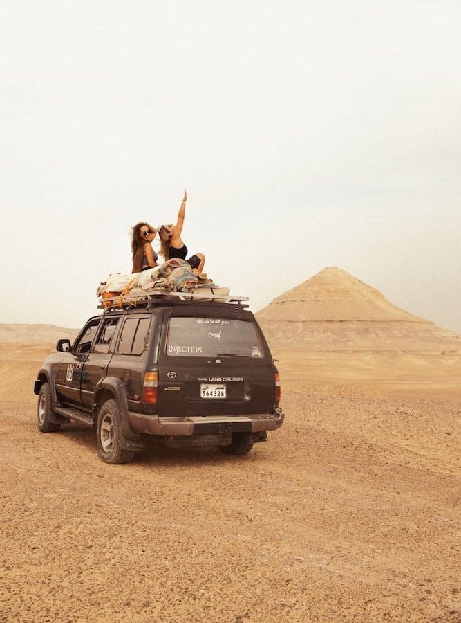 Two girls sitting on top of a Jeep in Egypt's West Desert with Pyramid Mountain in the background.