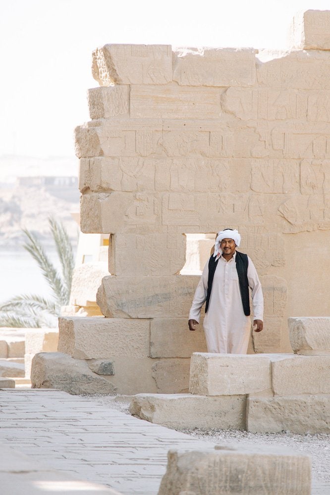A man in traditional white Egyptian robes smiles at the temple of Isis in Aswan, Egypt.