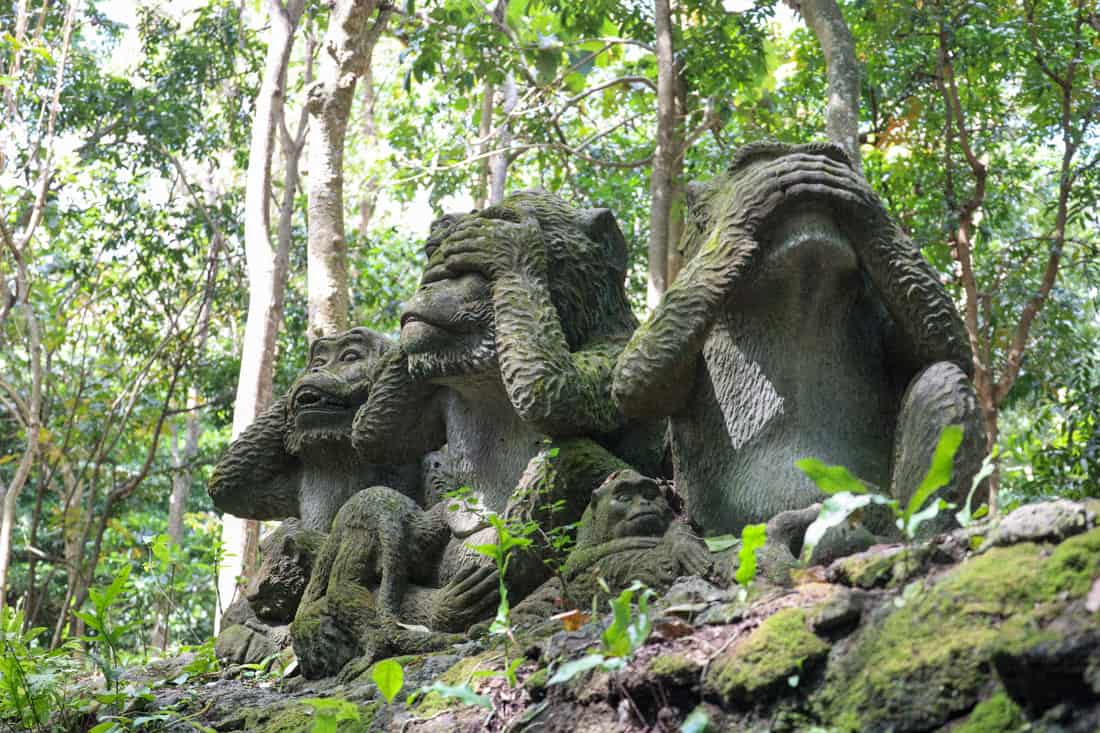 Moss covered stone statues of monkeys at the Ubud Monkey Forest covering theri eyes.