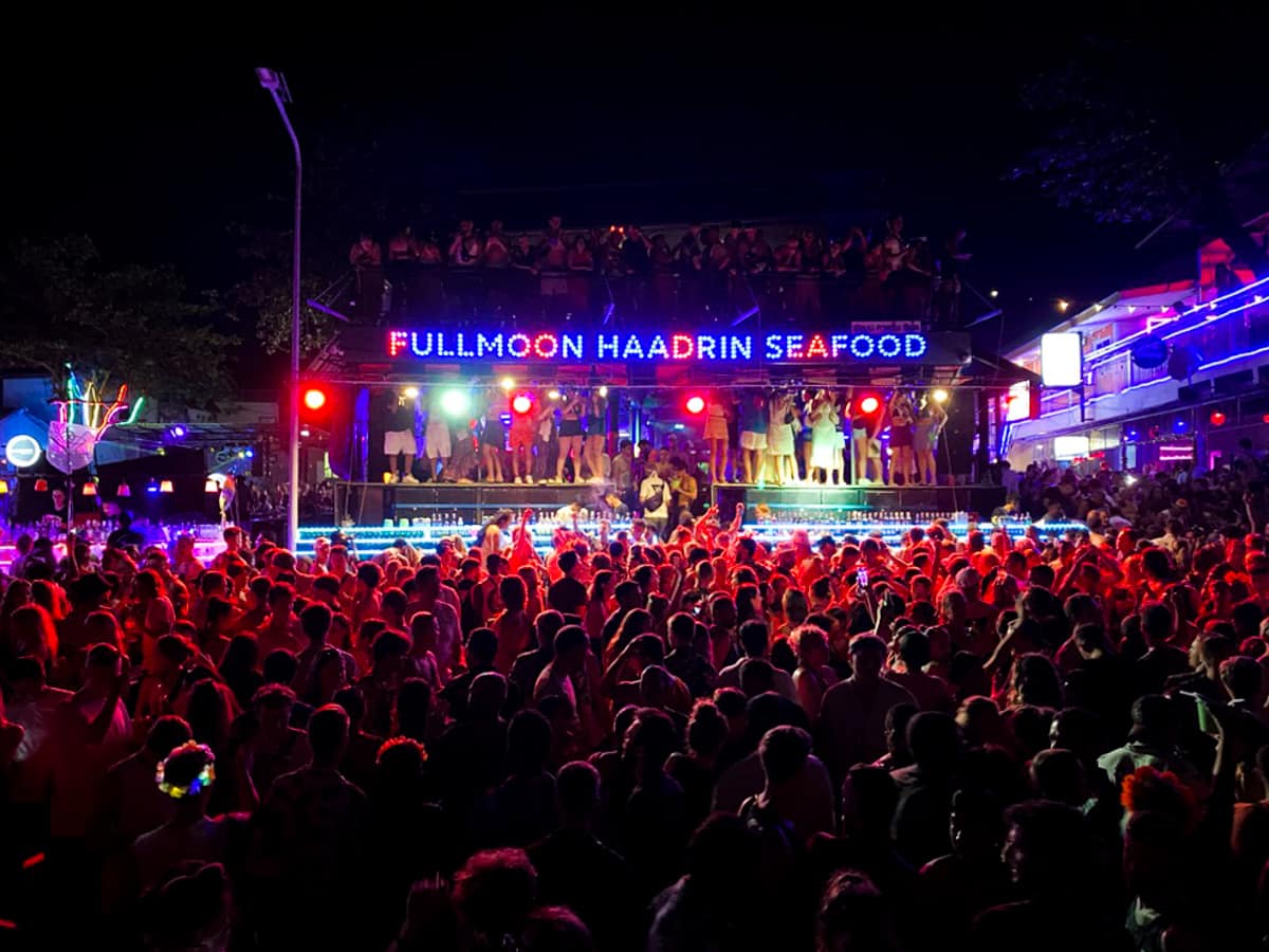 A large crowd of people is illuminated by a red light. On the stage in the background, you can see a sign saying Full Moon Haadrin Seafood.