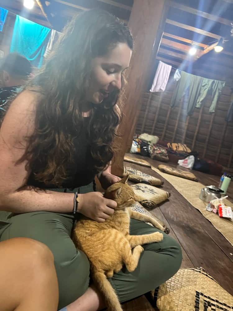 Blogger Katie Caf poses with an orange cat while having dinner at a traditional guest house at Wae Rebo.