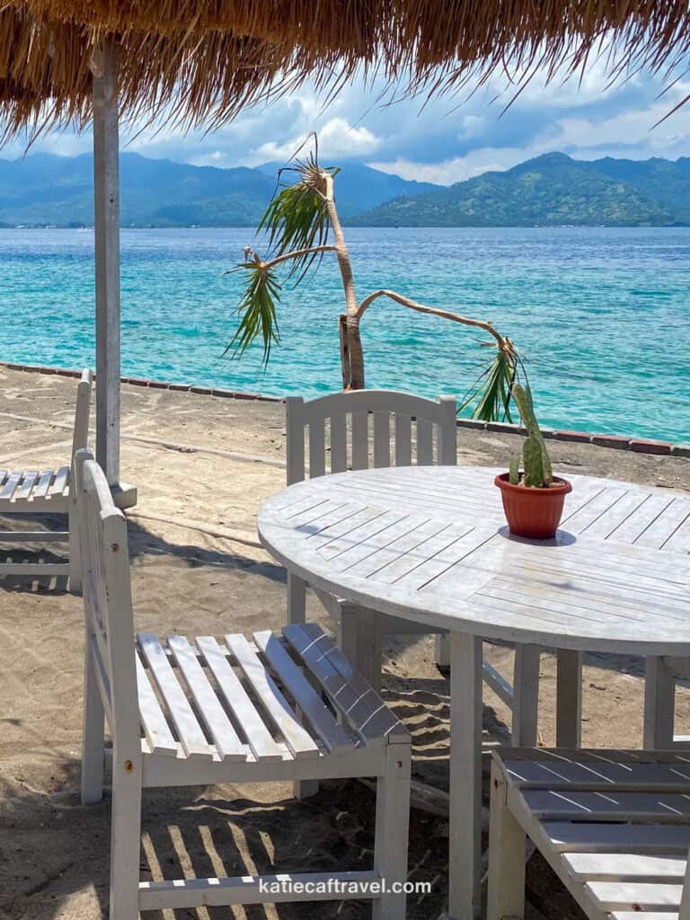 A white table in front of a beach with bright blue water under a straw canopy on Gili T.