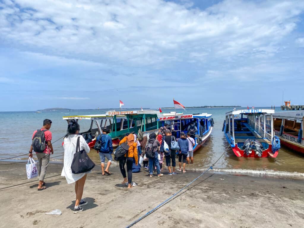 A row of small boats along the beach on Lombok Island in Indonesia. You can see passengers lining up on the beach to enter.