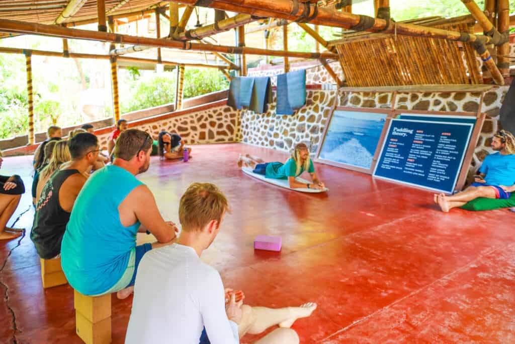 A class sitting around teaching a surf movement at a surf camp.