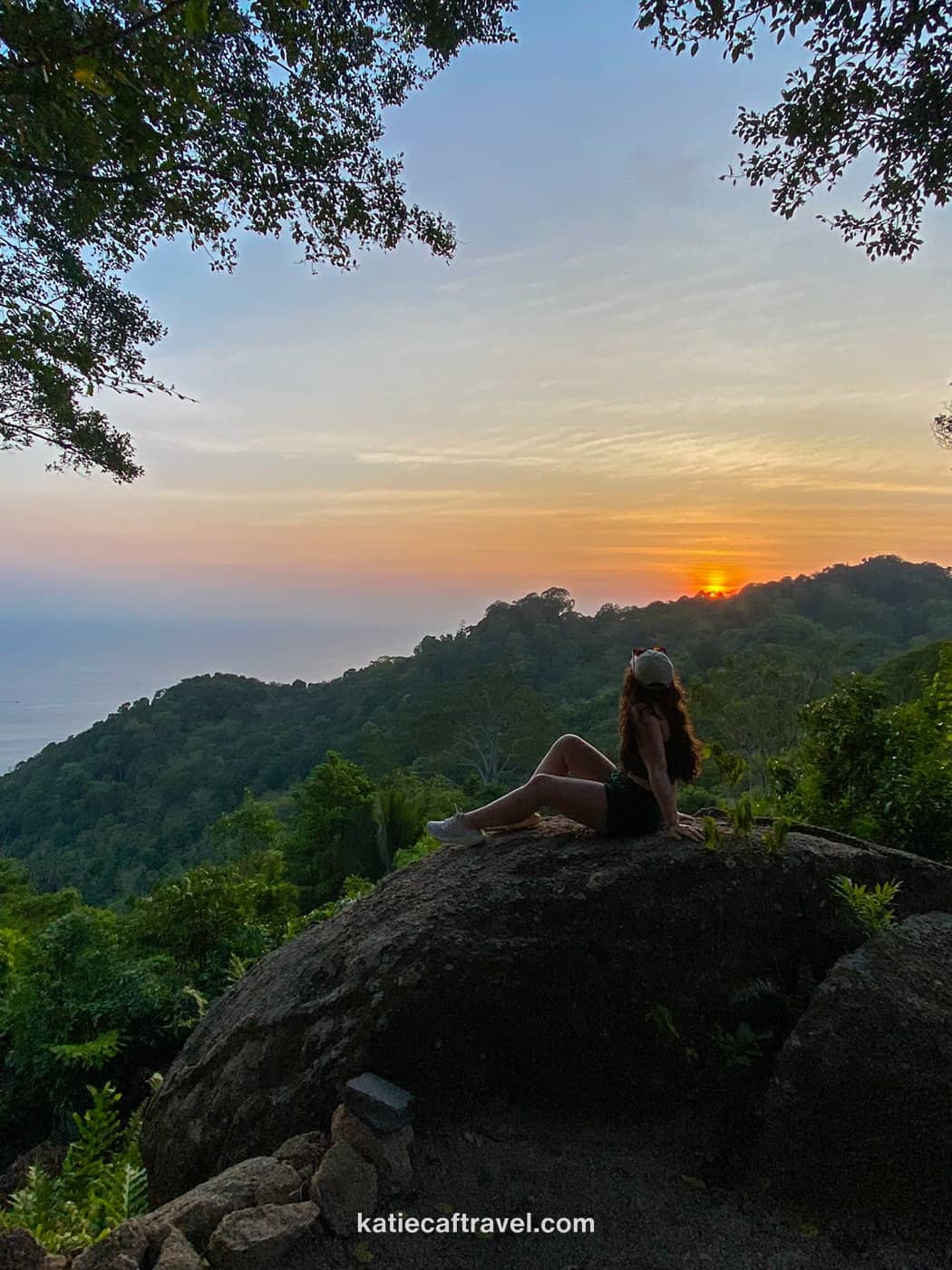 Travel blogger Katie Caf poses on a rock with the sunset behind her on Koh Tao island in Thailand.