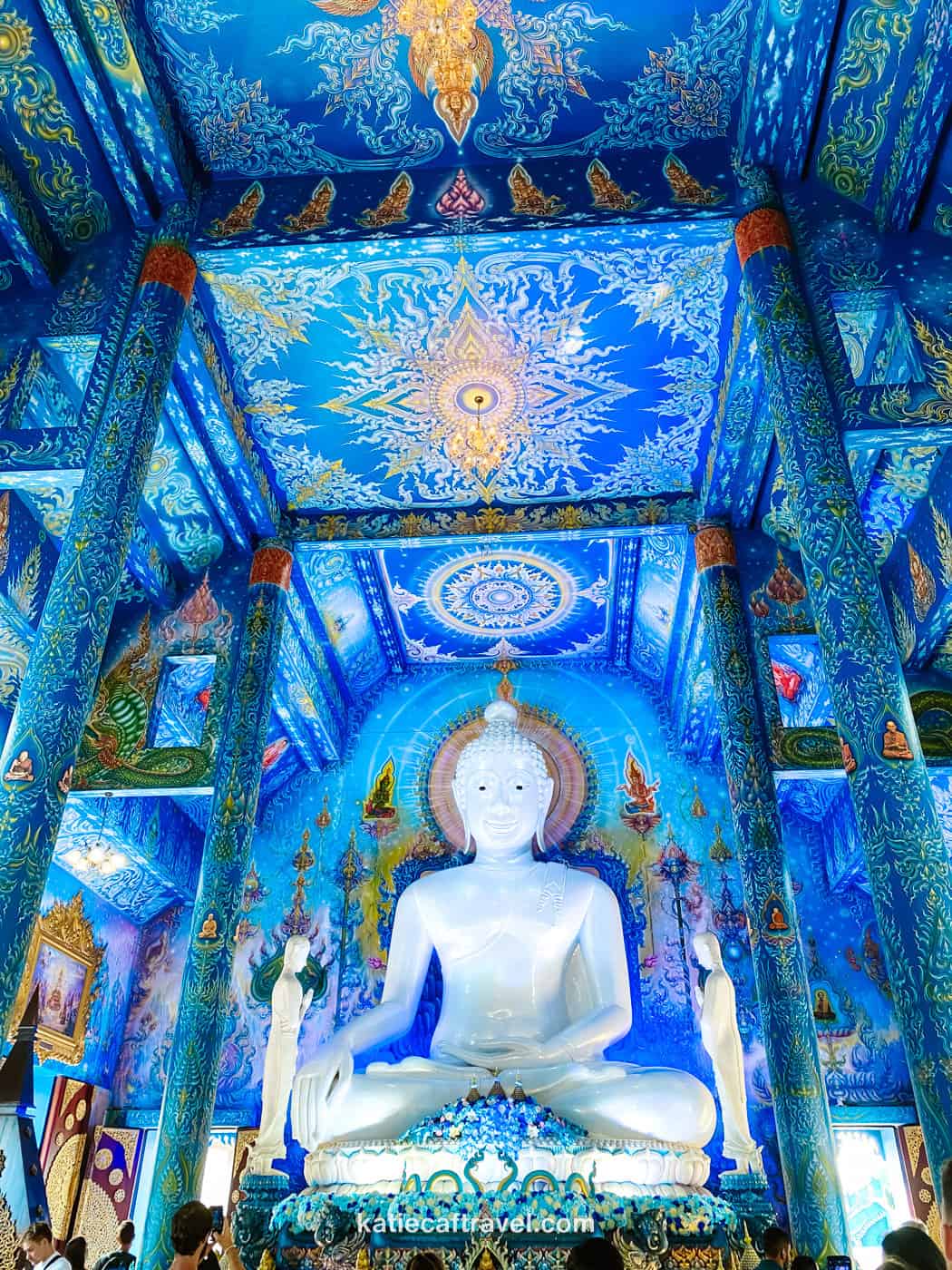 The interior of the Blue Temple in Chiang Rai, Thailand, featuring a large white buddha at the center of an intricately decorated blue room.