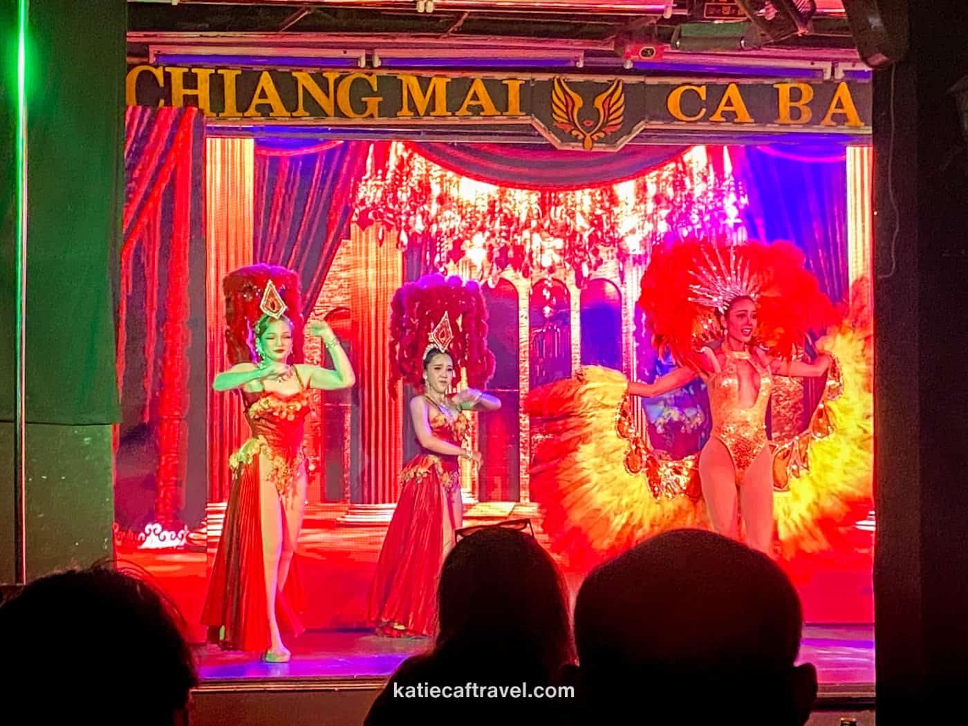A row of performers dressed in red with elaborate feathered outfits at a ladyboy cabaret in Chiang Mai, Thailand.
